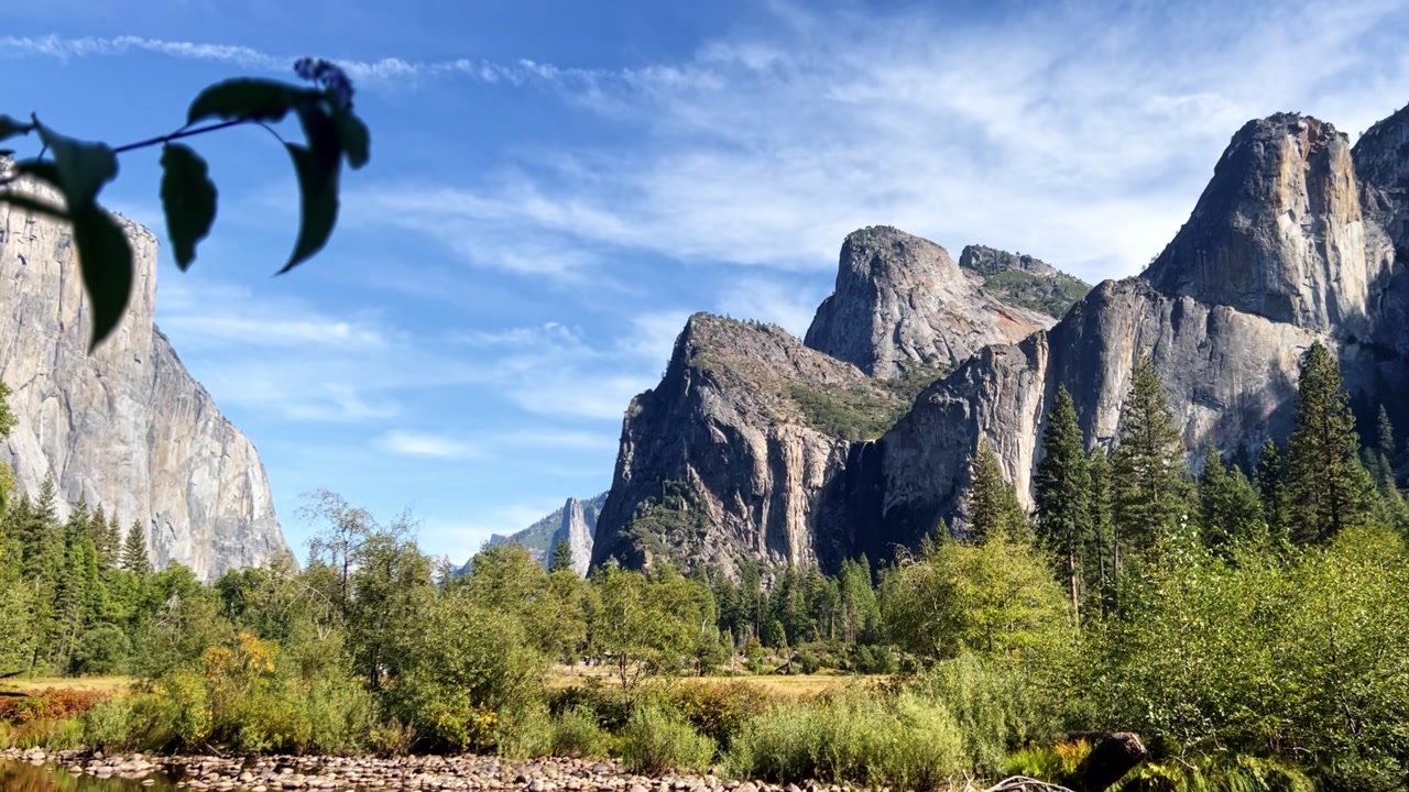 View of the Three Brothers and Bridalveil Fall in Yosemite National Park, with forest elements and leaves adding depth to the scene.