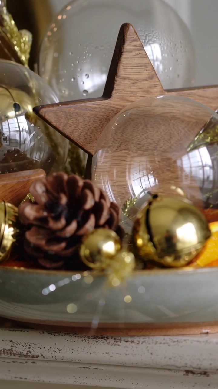 Video verticale: Telecamera in movimento che solleva una ciotola festiva sul caminetto, mettendo a fuoco una stella di legno e una sfera di vetro.