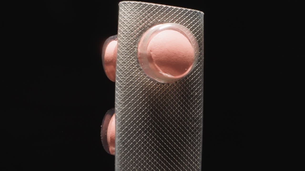 ampolla plateada curva con píldoras rosadas sobre fondo negro