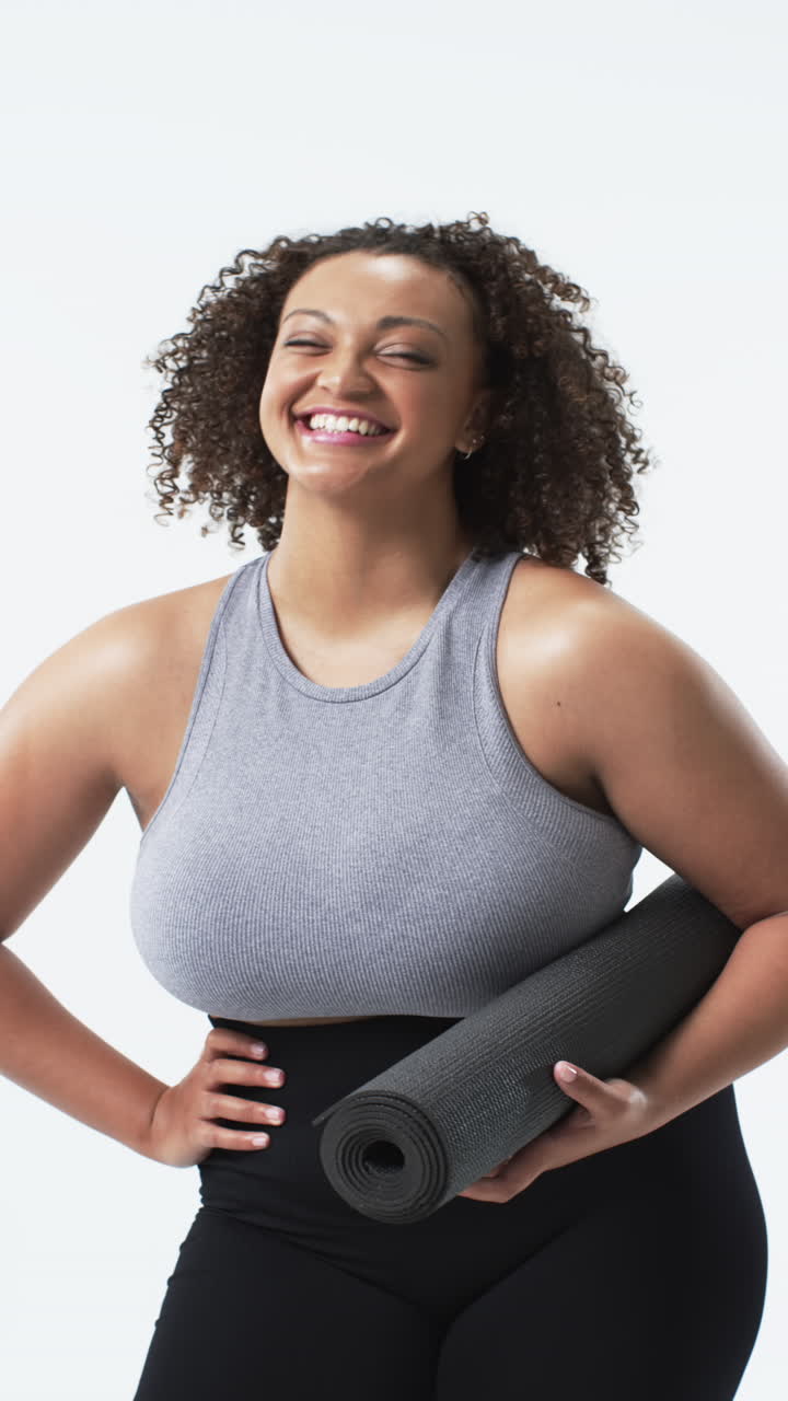 Video verticale: Donna curvy sorridente che tiene un tappetino da yoga, promuovendo la positività corporea e il fitness.