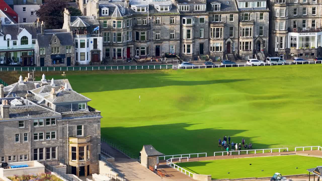 Drone pans across iconic golf course, historic clubhouse, and fairway under bright daylight conditions