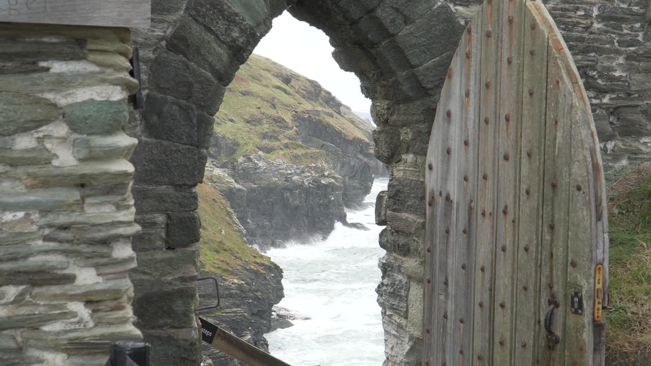 Close up view of one of the Tintagel Castle is a medieval fortification located on the peninsula of Tintagel, Cornwall. Passageway with old door that show the waves hitting the coast. 4K