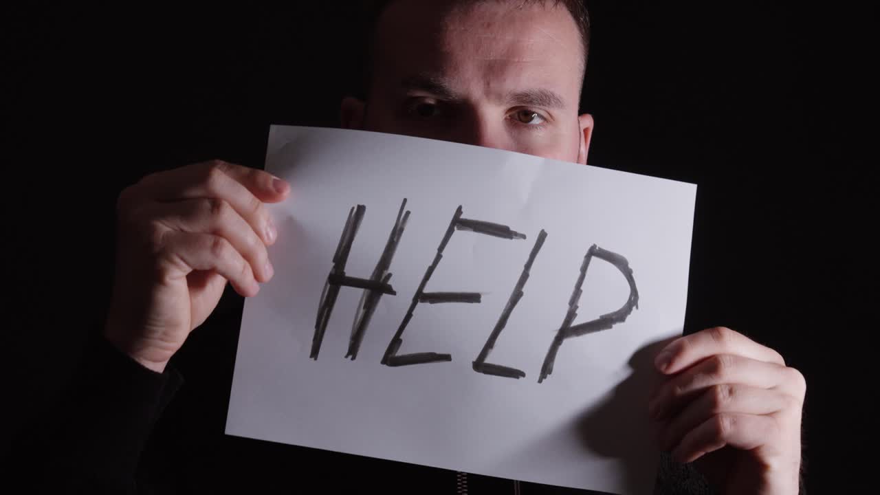 Close-up of a man holding a “help” sign, symbolizing mental health struggles and need for support