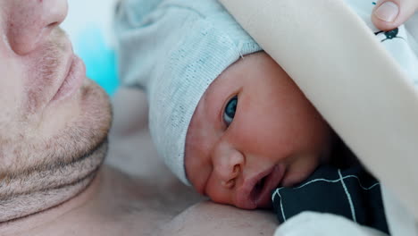 cute face of a newborn looking with one opened eye. child lies on the naked dad's chest. close up.