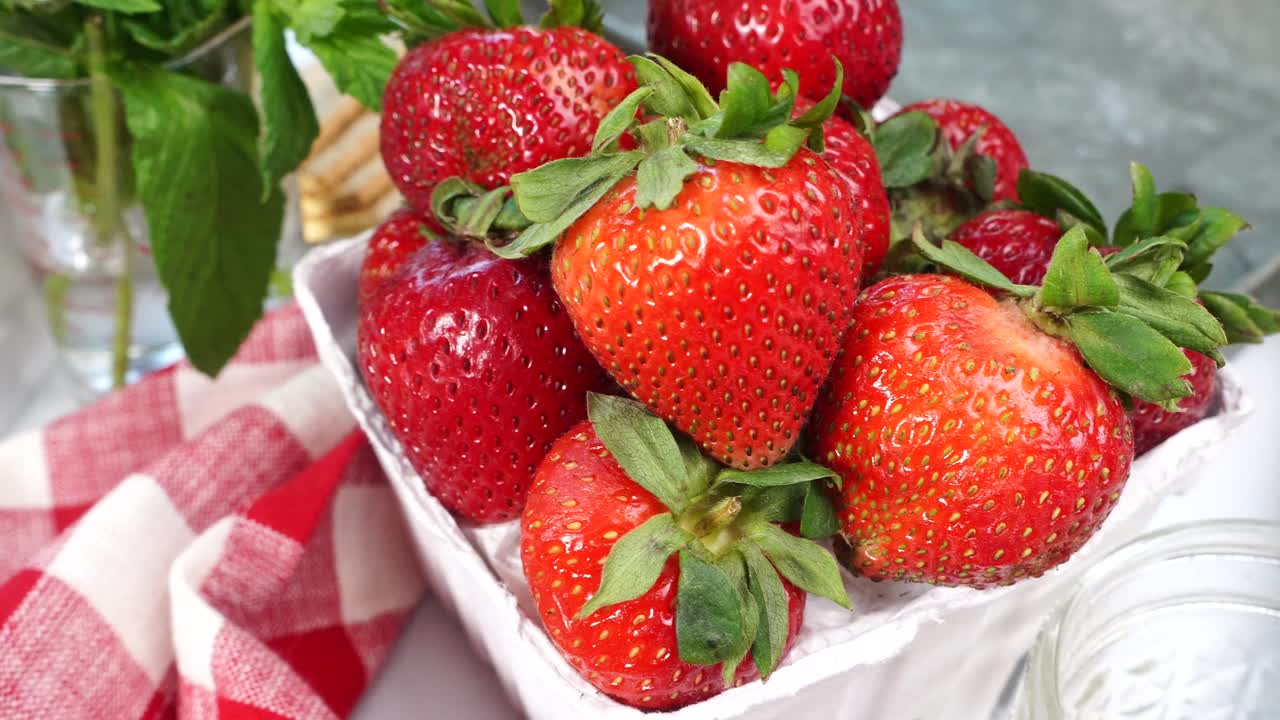 Close up of video moving across fresh red strawberries and crushed graham crackers in a mason jar and on a white plate. Making a strawberry shortcake martini for a party. Fresh fruit for dessert.