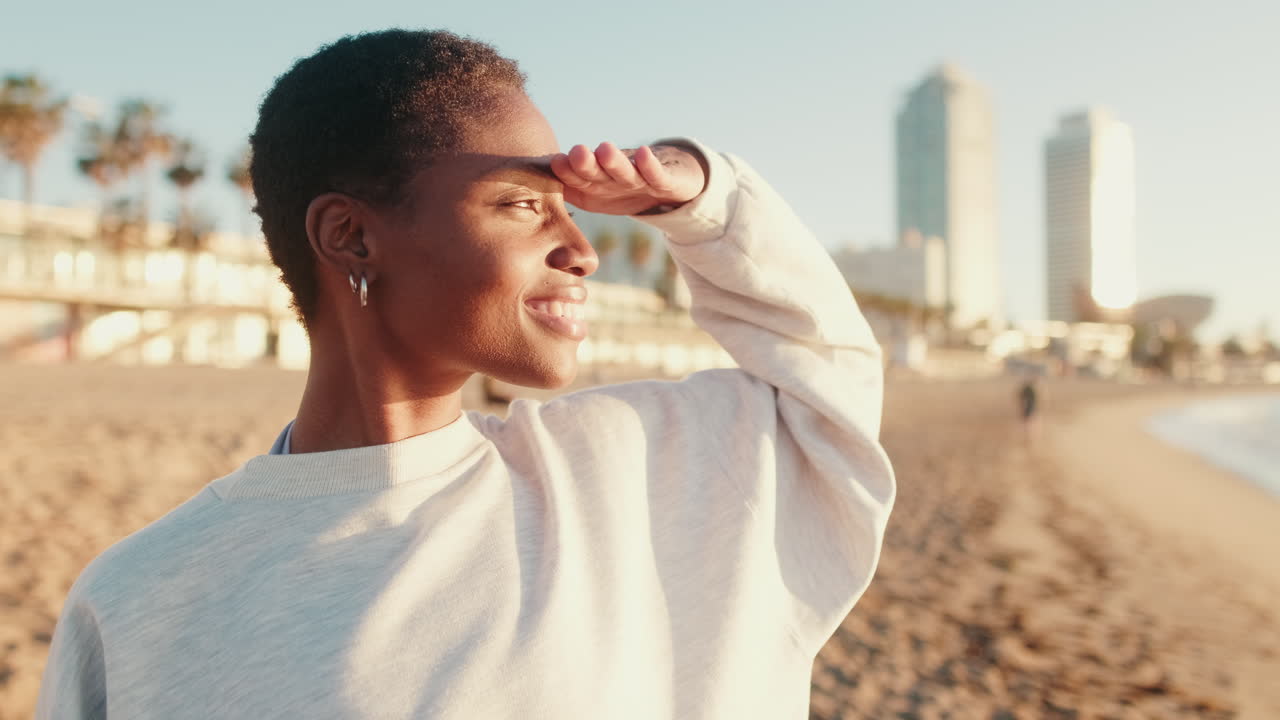 Jeune femme afro-américaine souriant et regardant au loin sur une plage ensoleillée