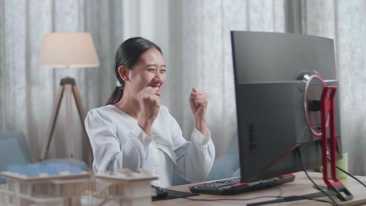 집에서 데스크에서 일하는 동안 집 모델과 함께 축하하는 아시아 여성 엔지니어