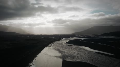 aerial thor valley, flying over glacial river flowing through black volcanic floodplain, thorsmörk dramatic moody landscape iceland