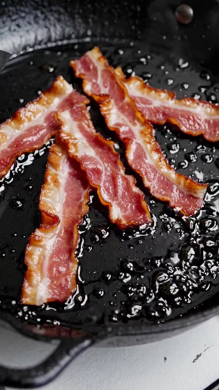 Bacon croccante che frigge in una padella di ghisa nera