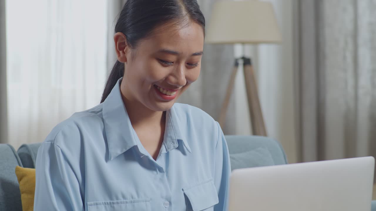 거실 의 소파 에 앉아 노트북 컴퓨터 에서 타이핑 하는 미소 짓는 아시아 여자 의 근접 사진