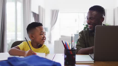 African-american-father-and-son-doing-homework-and-using-a-laptop-together