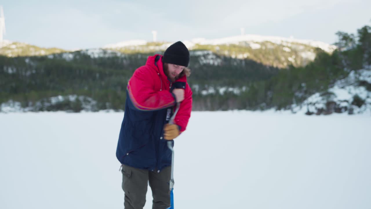 An Ice Fisherman With A Hand Auger Drilling A Hole In Frozen Lake