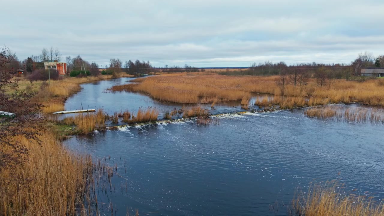 Drone advances above Pape Lake outlet revealing winding canal and tranquil wetland rapids.