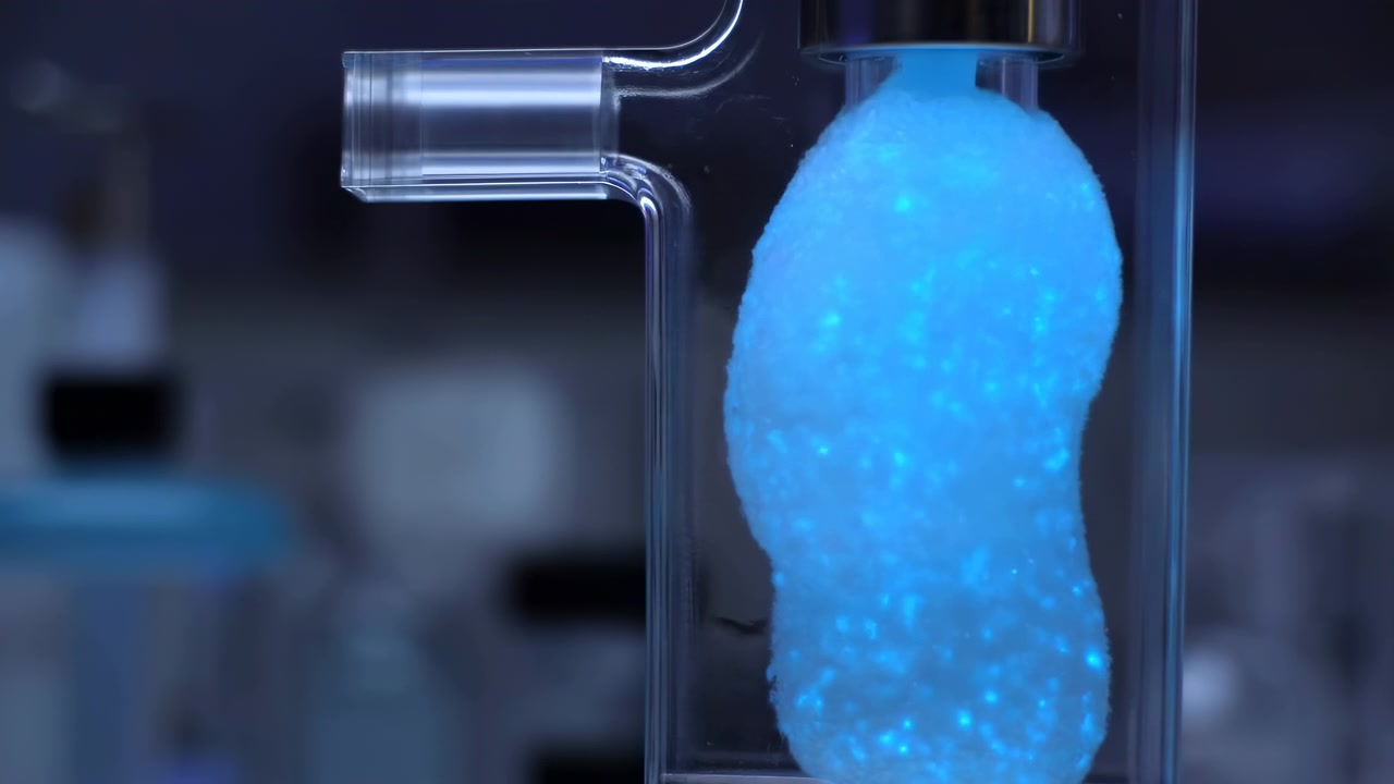 Glowing porous pellet inside vertical glass tube appears to brighten from soft blue to vivid luminescence inside sterile laboratory setting, creating subtle moving reflections and cool clinical mood
