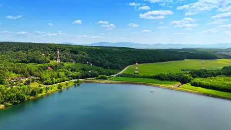 tranquil lake and green land. a peaceful lake reflects the sky, surrounded by lush greenery and distant mountains on a clear sunny day