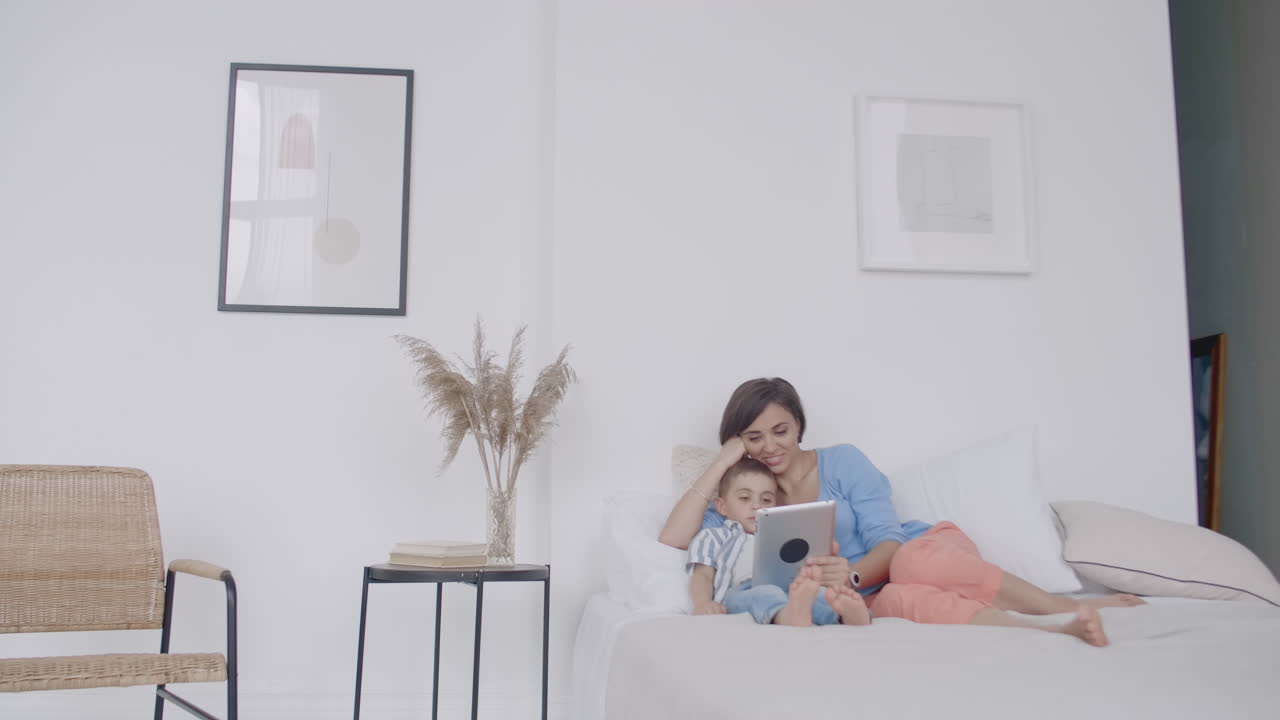 madre joven feliz mostrando dibujos animados en una tableta digital a su hijo pequeño antes de irse a dormir. madre feliz mostrando caricaturas en una tablet digital a su niño pequeño