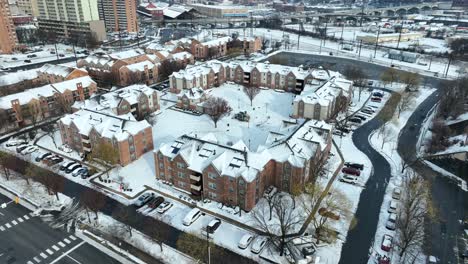 Snow-covered-residential-complex-with-brick-buildings-and-parked-cars,-urban-backdrop