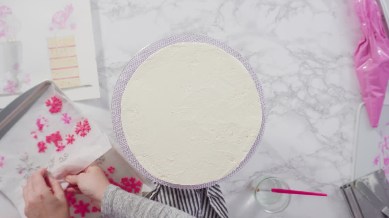 decorando el pastel funfetti redondo con copos de nieve de fondante rosado y blanco.