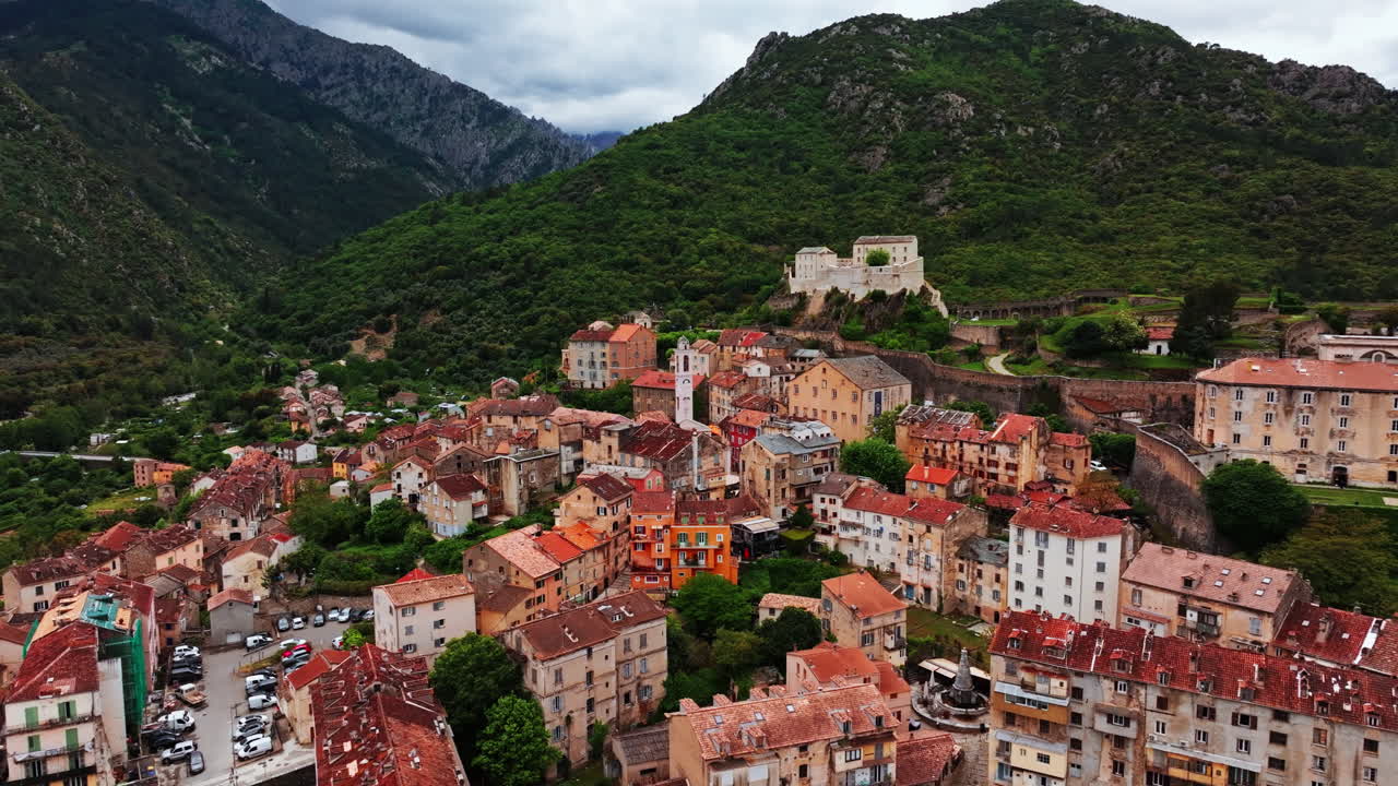 Aerial drone shot over the historic town of Corte, Corsica, France. High view of the old town and fortress overlooking the landmark on top of the hill. View of the scenic landscape and mountains