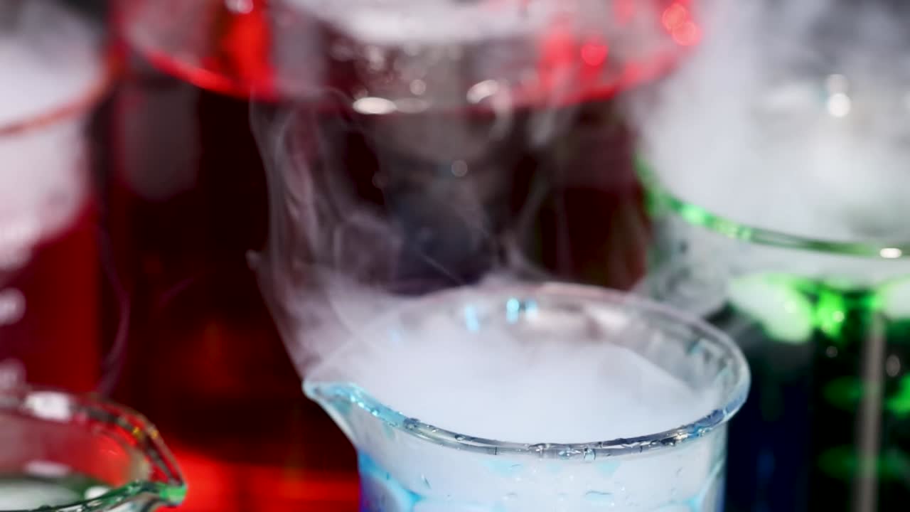 Close-up of beakers with colorful liquids emitting vapor, showcasing a dynamic chemical reaction.