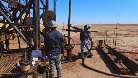 man in helmet hits the nut with a sledgehammer. setting the metal equipment for drilling oil or gas.