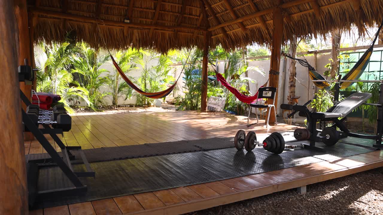 An outdoor gym with weights, a bench, and hammocks under a tropical thatched roof