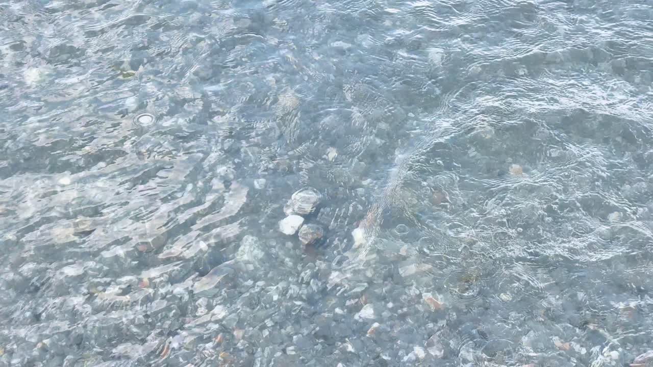 A rock is thrown into a clear lake, creating a splash and expanding water ripples