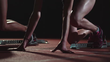 female runners at athletics track crouching at the starting blocks before a race. in slow motion.