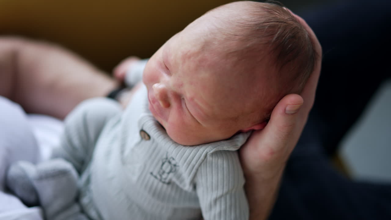 Baby boy cries lying on the big hand of his dad. Newborn makes a wry face and then calms down. Close up.