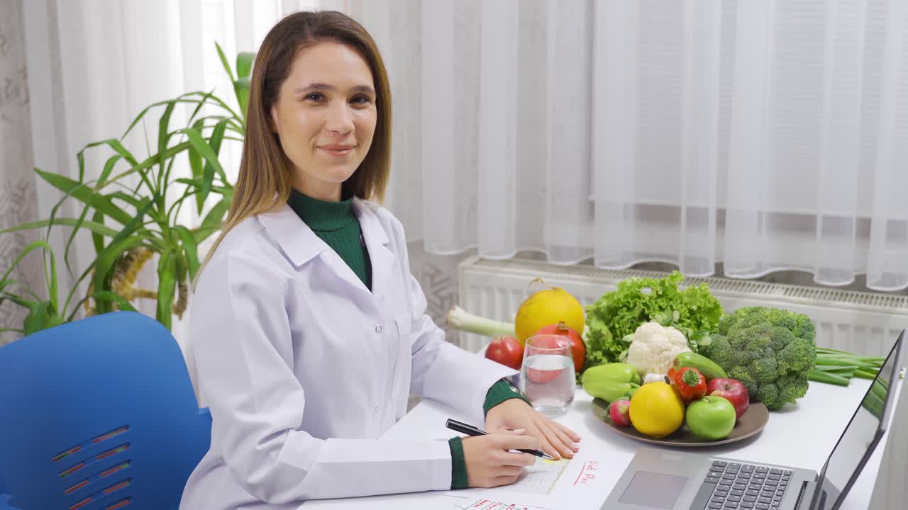 nutricionista mujer positiva trabajando en una mesa llena de verduras y sonriendo mirando a la cámara.