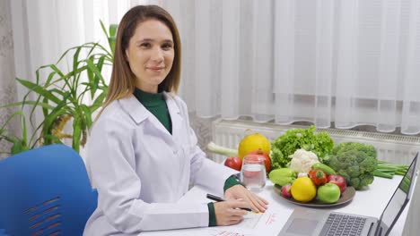 nutricionista mujer positiva trabajando en una mesa llena de verduras y sonriendo mirando a la cámara.