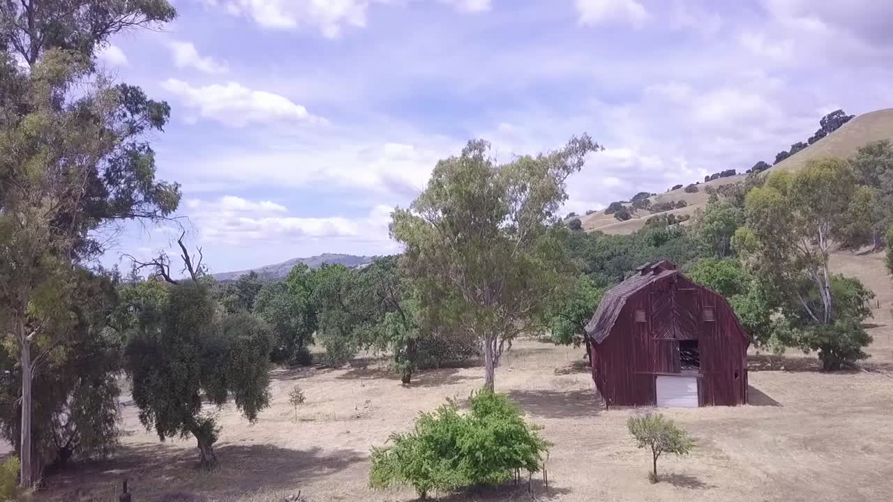 toma aérea en movimiento del granero rojo en el campo, que se eleva para revelar las tierras de cultivo circundantes y el cielo azul con nubes