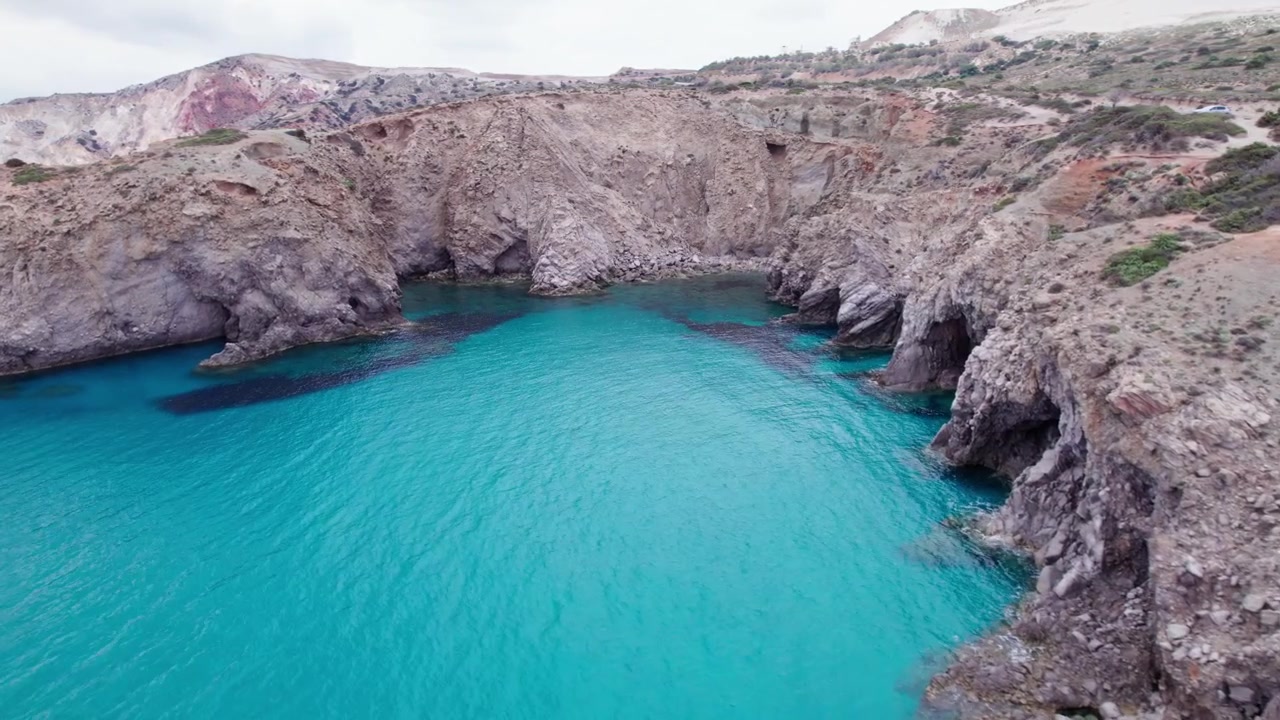 Spettacolari riprese aeree con drone di grotte marine naturali uniche e un arco di roccia vulcanica lungo la costa mozzafiato e frastagliata di Milos, Grecia, circondate da acqua cristallina color turchese.