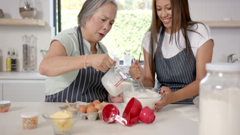 pouring milk, asian grandmother baking with granddaughter mixing batter in kitchen