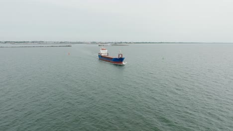 Aerial-establishing-view-of-large-blue-cargo-ship-leaving-Port-of-Liepaja-,-Karosta-bridge,-slight-overcast-day,-calm-Baltic-sea,-wide-tracking-drone-shot