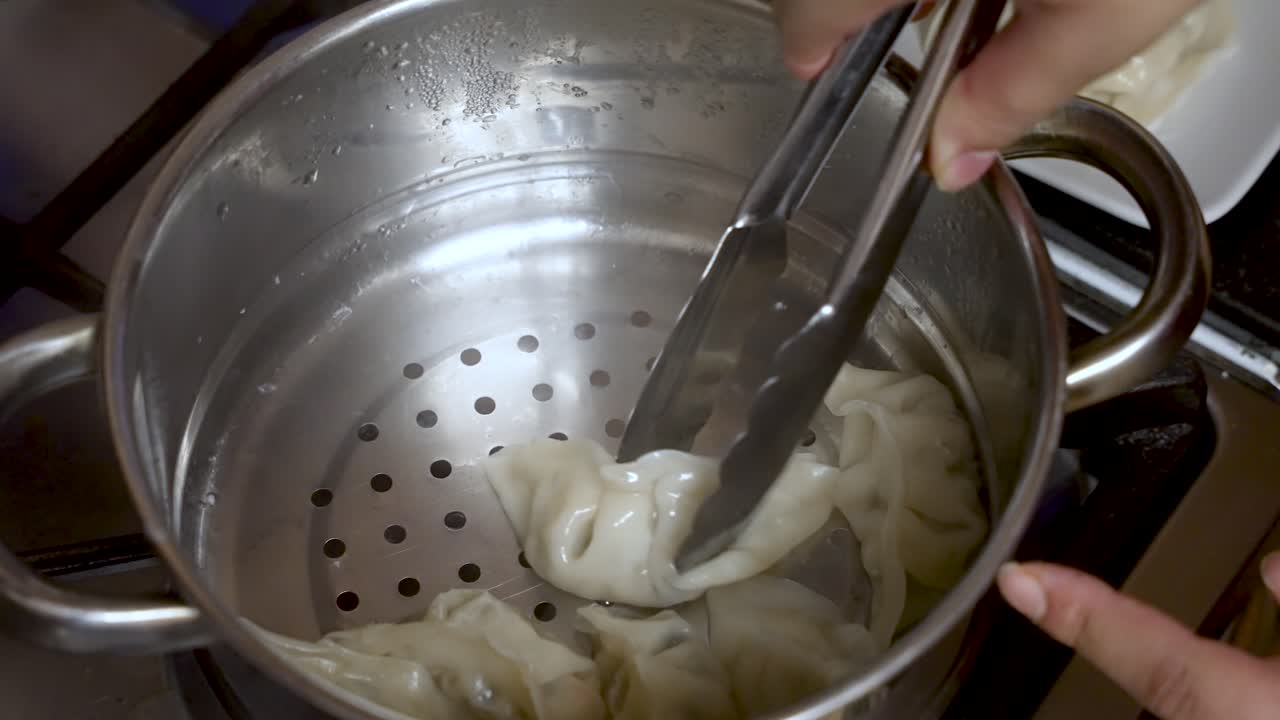 A cooking chef uses a metal grabber to retrieve dumplings from a metal bowl, epitomizing the art of culinary preparation and food crafting