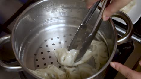a cooking chef uses a metal grabber to retrieve dumplings from a metal bowl, epitomizing the art of culinary preparation and food crafting
