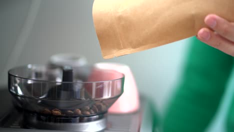 Crop-person-pouring-coffee-beans-from-paper-bag-into-grinder