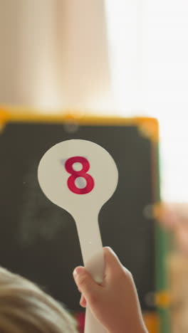 little boy shows digit on plastic tag while girl stands near blackboard at home closeup. brother and sister play school and learn maths lesson