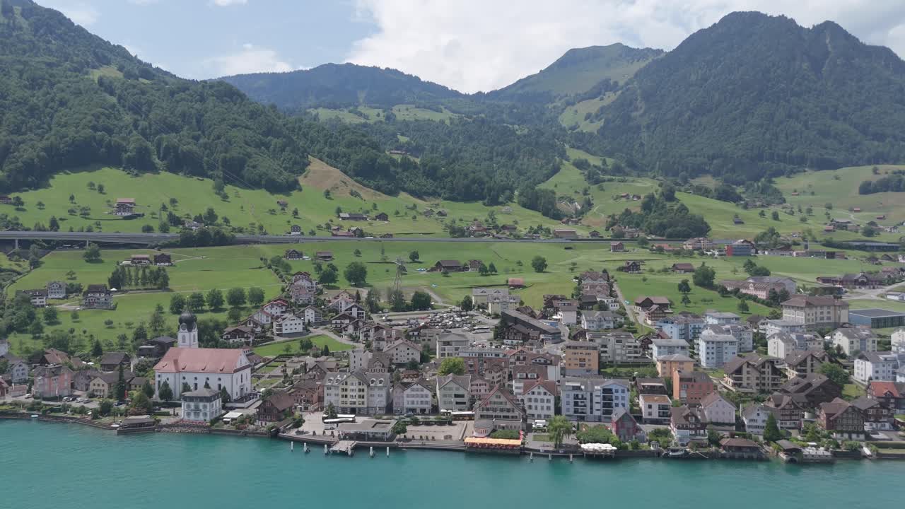 Ripresa aerea con drone di Beckenried, Svizzera, sul Lago di Lucerna, che mostra una cittadina lacustre con colline verdi, pendii alpini e case sul lungomare in una limpida giornata estiva