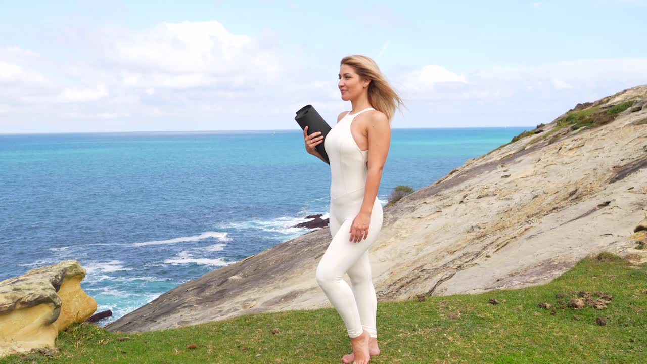 Happy Woman Standing on Cliff with Yoga Mat Overlooking Ocean