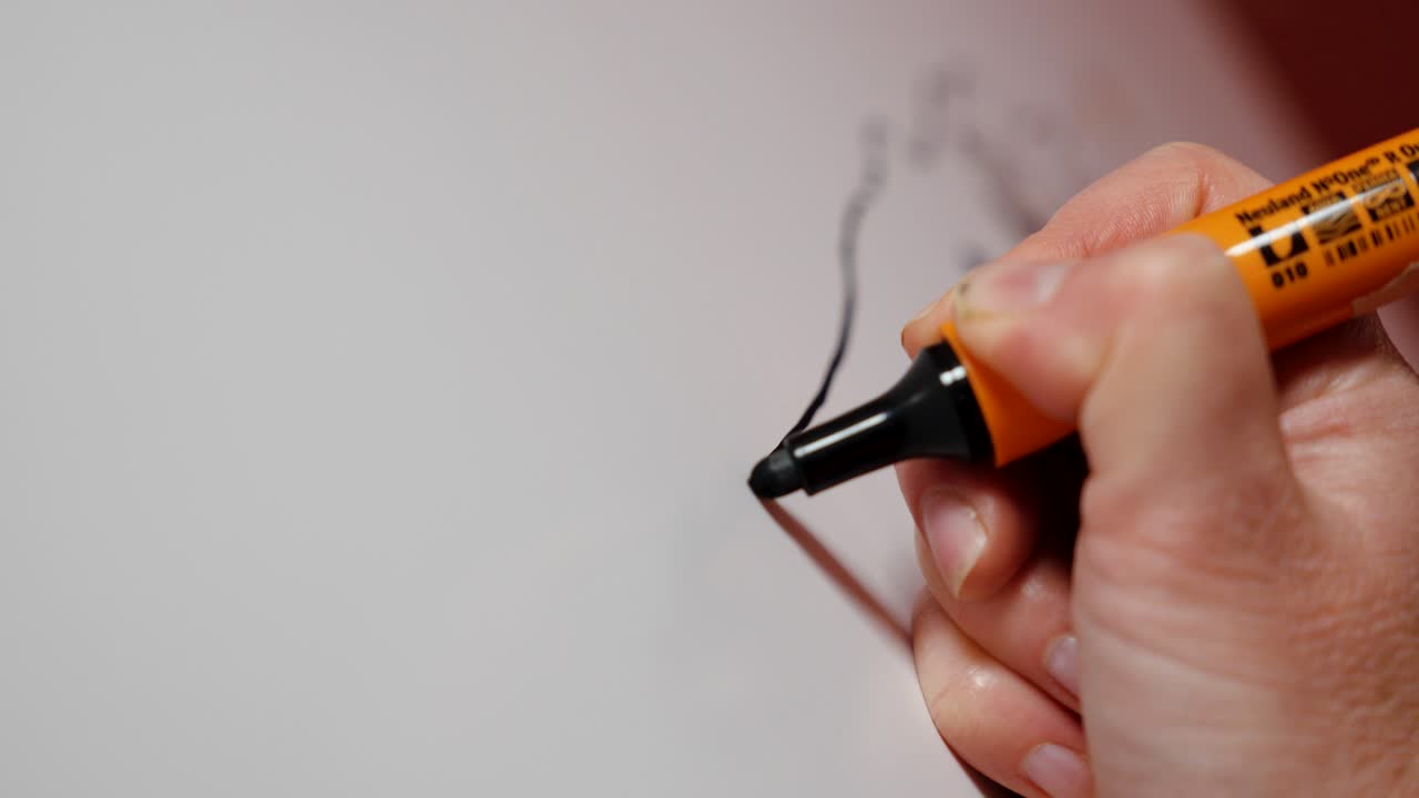 close-up shot of an artist using a black marker pen to create art on a whiteboard
