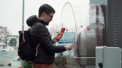 hombre usando un teléfono público en un día de lluvia