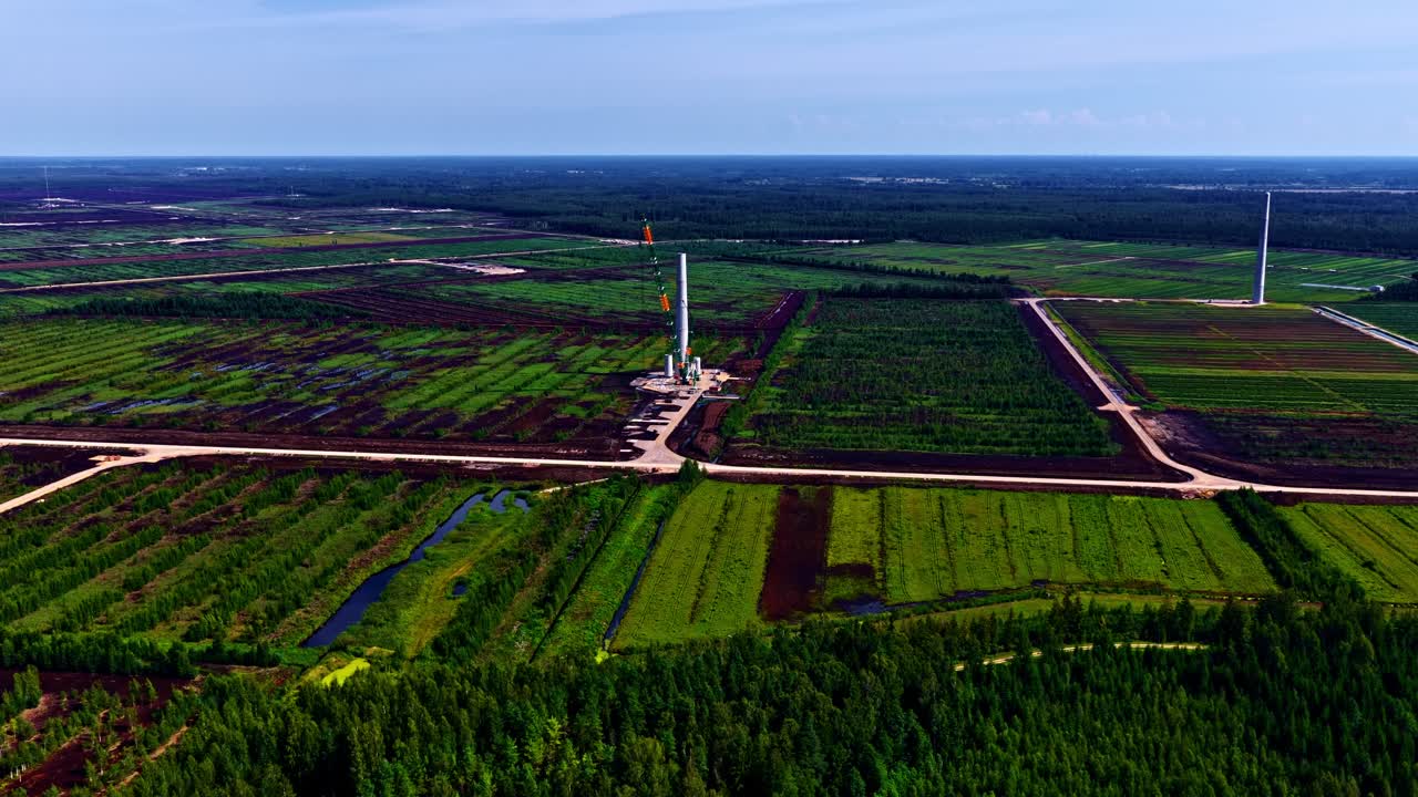 Crane building single wind turbine in vast fields with path cutting through landscape