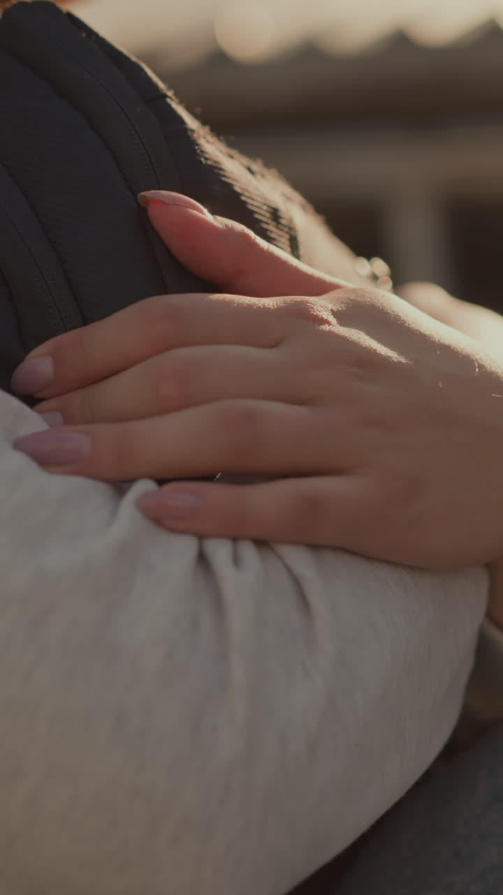 primer plano de las manos de individuos con uñas bien pulidas abrazando fuertemente una bolsa mientras la luz del sol se refleja suavemente en su piel, creando una atmósfera cálida y contemplativa