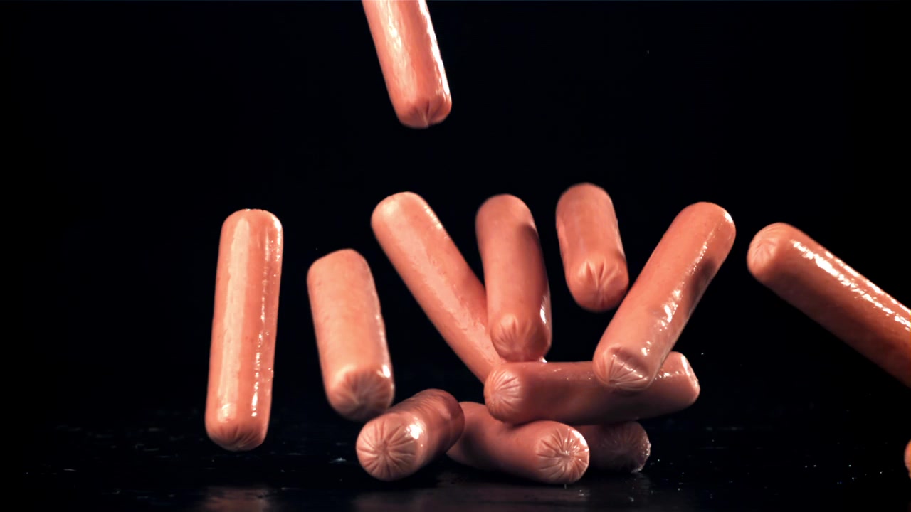 Salsicce crude che cadono in super slow motion su sfondo nero
