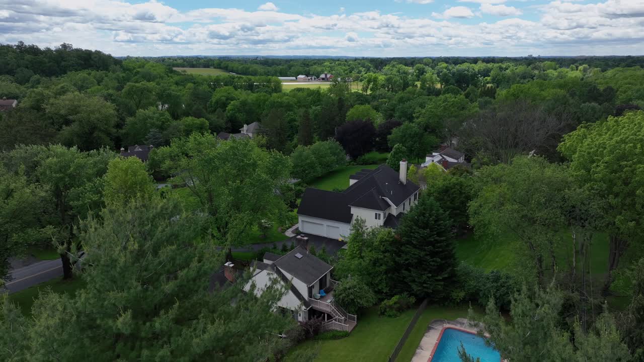 Green trees in upper class housing area with large houses and swimming pool in garden. Suburb district of american town. Descend drone wide shot. Forest landscape and clouds at sky.