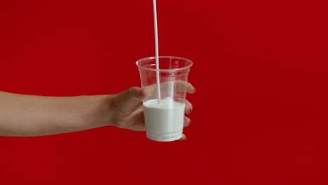 wide view of woman hands pouring milk into empty plastic glass in slow motion.