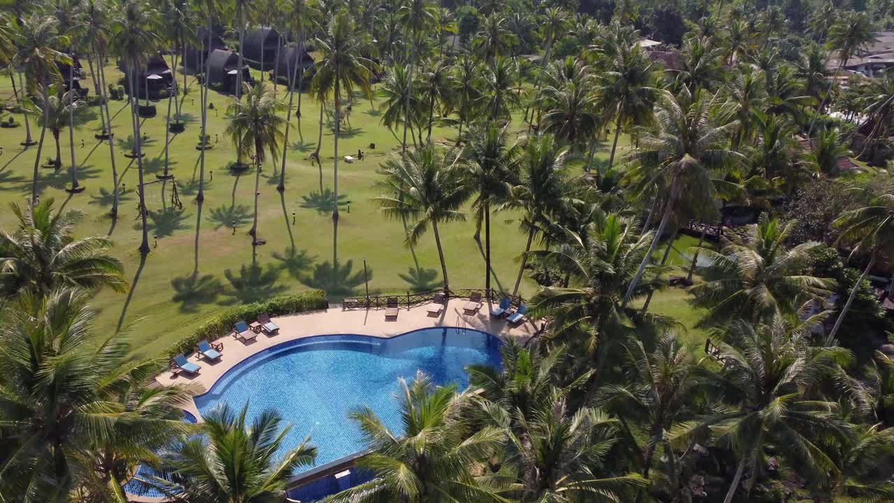 una piscina tropical con el sol reflejado en el agua, rodeada de palmeras y encantadores bungalows en el fondo, en un día azul claro y soleado en la isla de koh kood en tailandia en asia