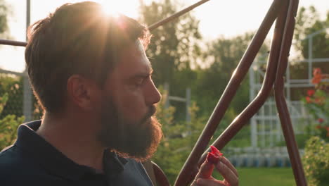 golden hour sunlight bathes man seated on swing bench savoring freshly picked strawberry with thoughtful expression while lush garden foliage and soft bokeh glow frame serene rural summer scene